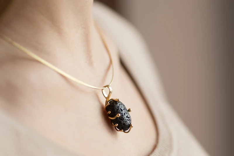 Gold pendant where the black lava stone is intricately embraced by a gold motif