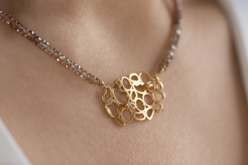 Necklace made of sapphires in earthy colors. The motif of the necklace is gold and depicts elaborate asymmetrical circles