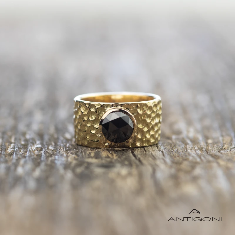 Gold hammered ring with a striking black diamond whose base is wide and embossed